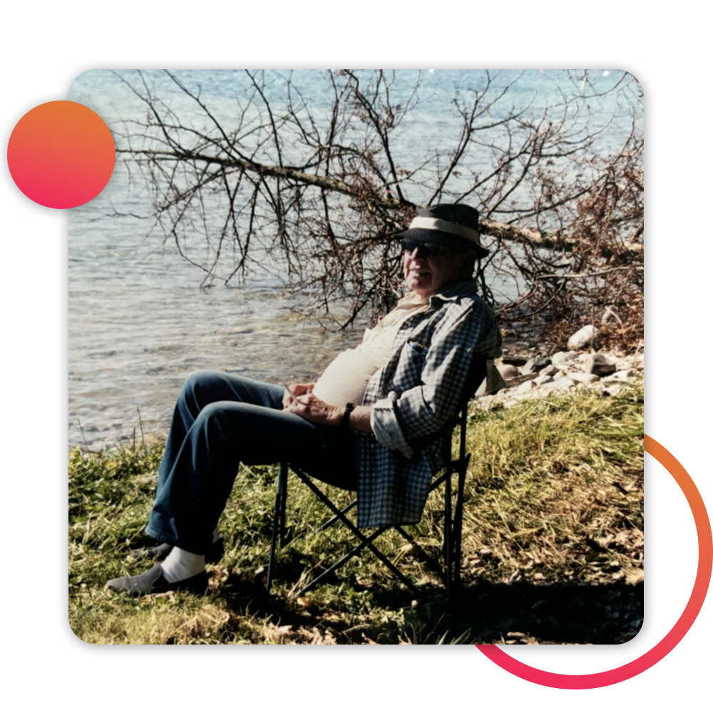 man in hat sitting lakeside, smiling at camera